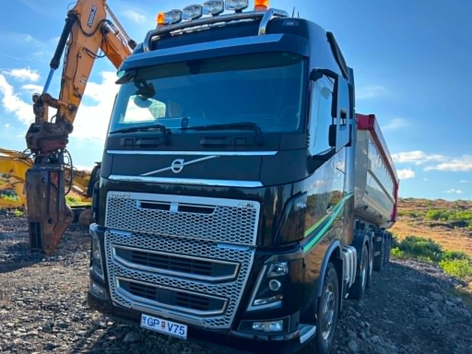 Volvo FH með fleyggröfu í bakgrunni